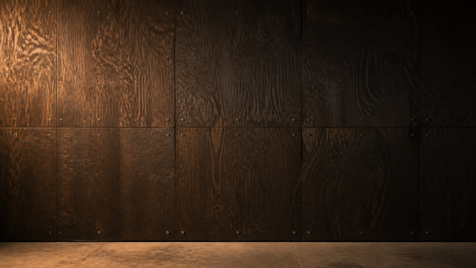 A dark plywood wall raked by one warm lamp