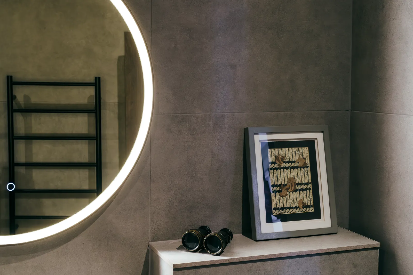 Bathroom with backlit round mirror, dark stone walls and black towel rail