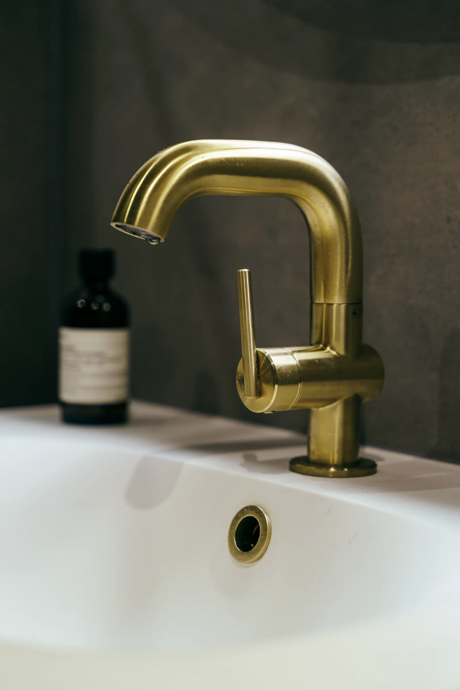 Brass basin mixer on a white basin with dark stone wall behind