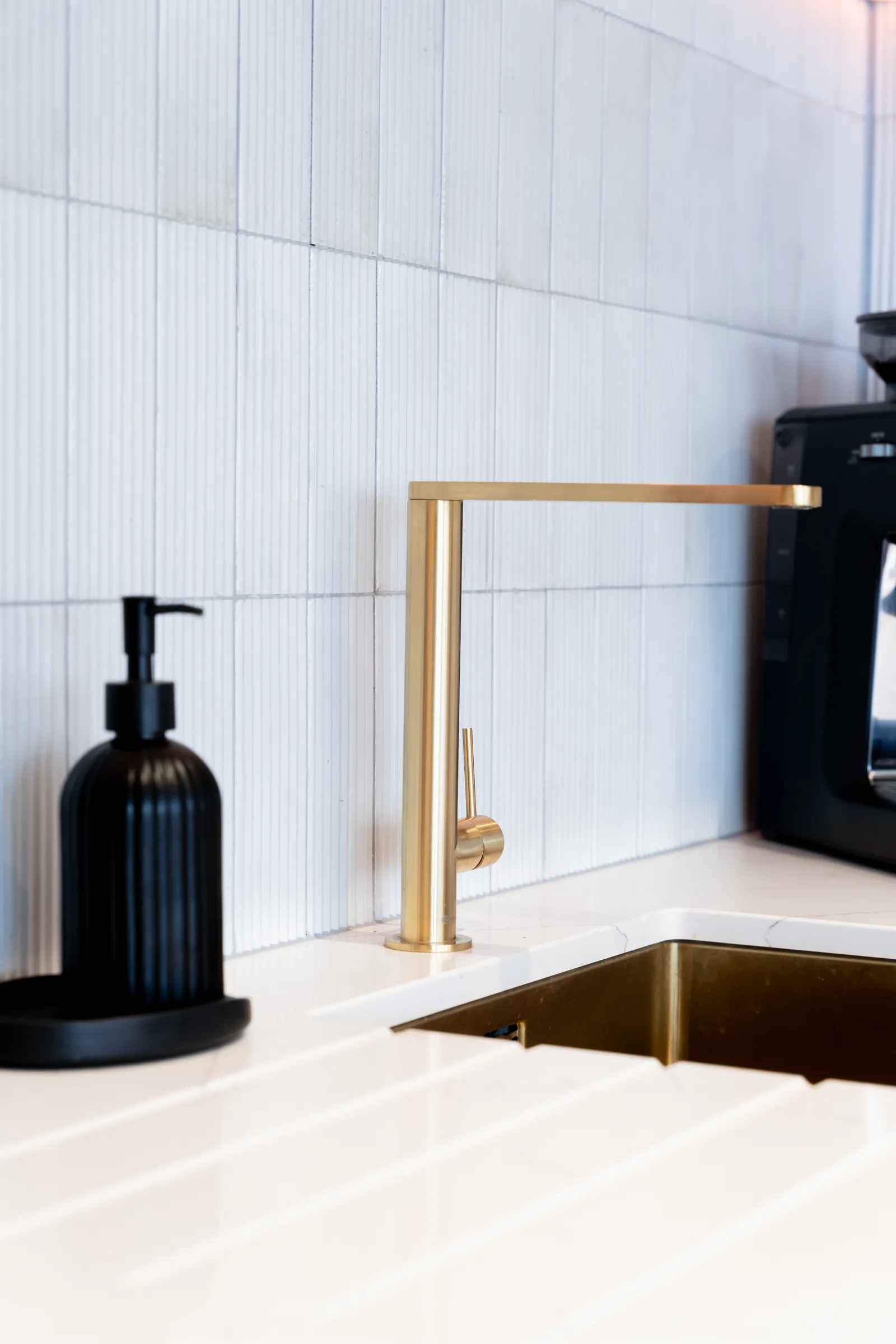 Brushed brass kitchen tap against a fluted white splashback
