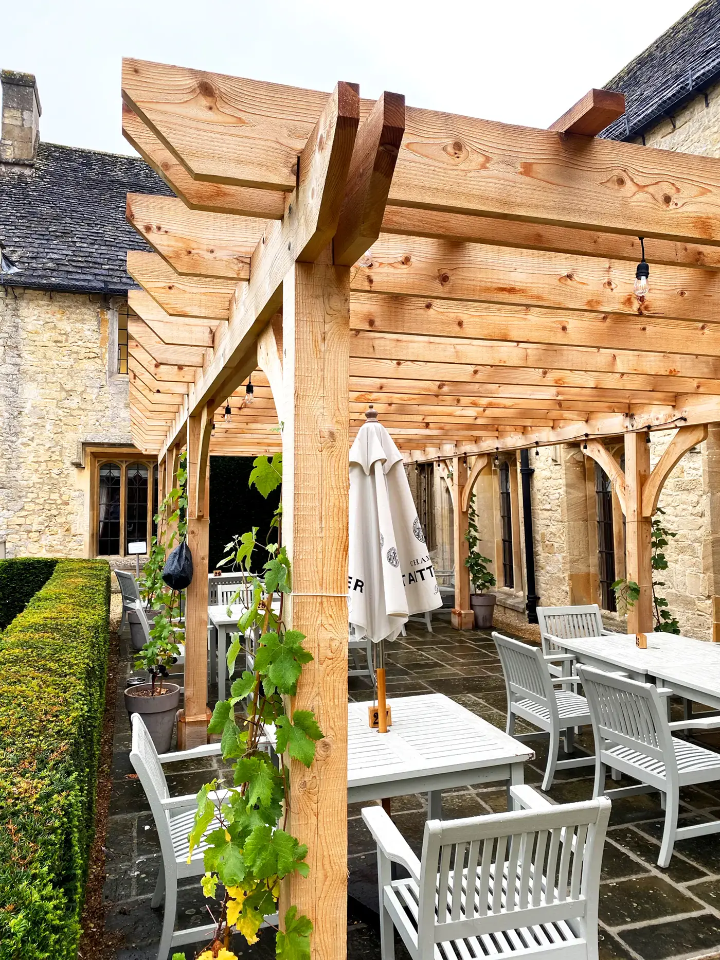 Oak pergola over an outdoor dining terrace beside a Cotswold stone house