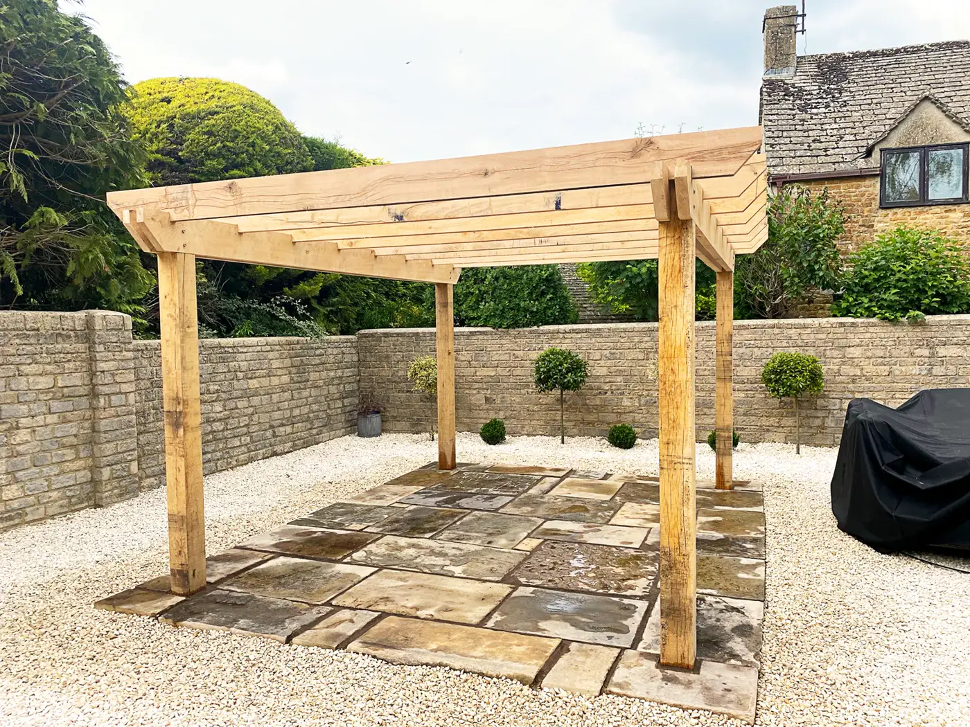 Timber pergola over a stone-paved area with clipped topiary