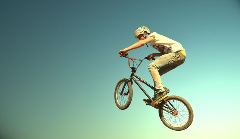 A rider in yellow suspended mid-air on a BMX against a flat teal sky, no ground visible
