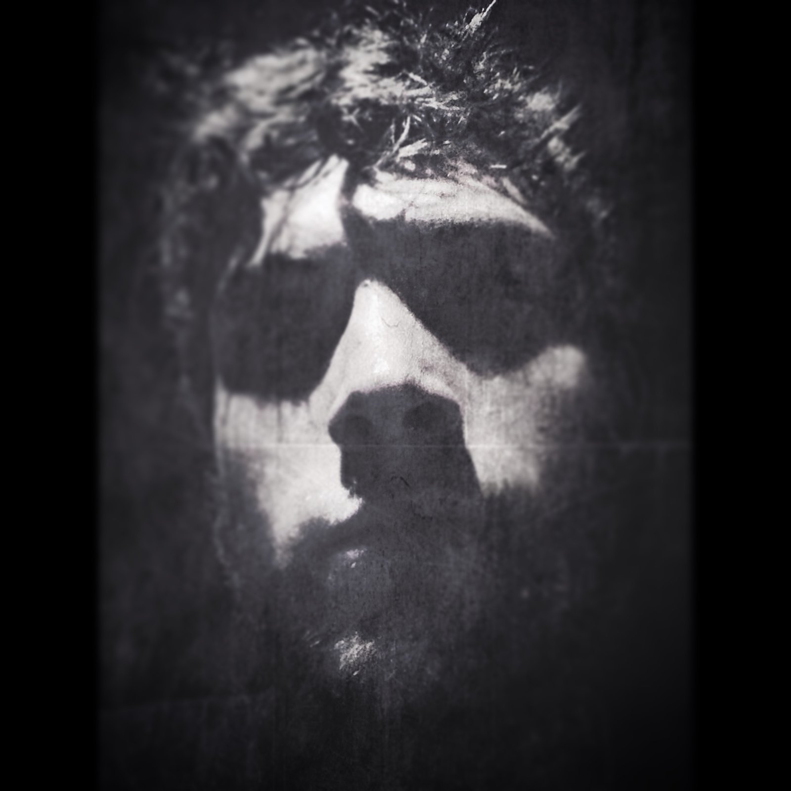 A heavily degraded black and white image of a bearded face with a crown of thorns, printed or projected onto a rough dark surface and photographed
