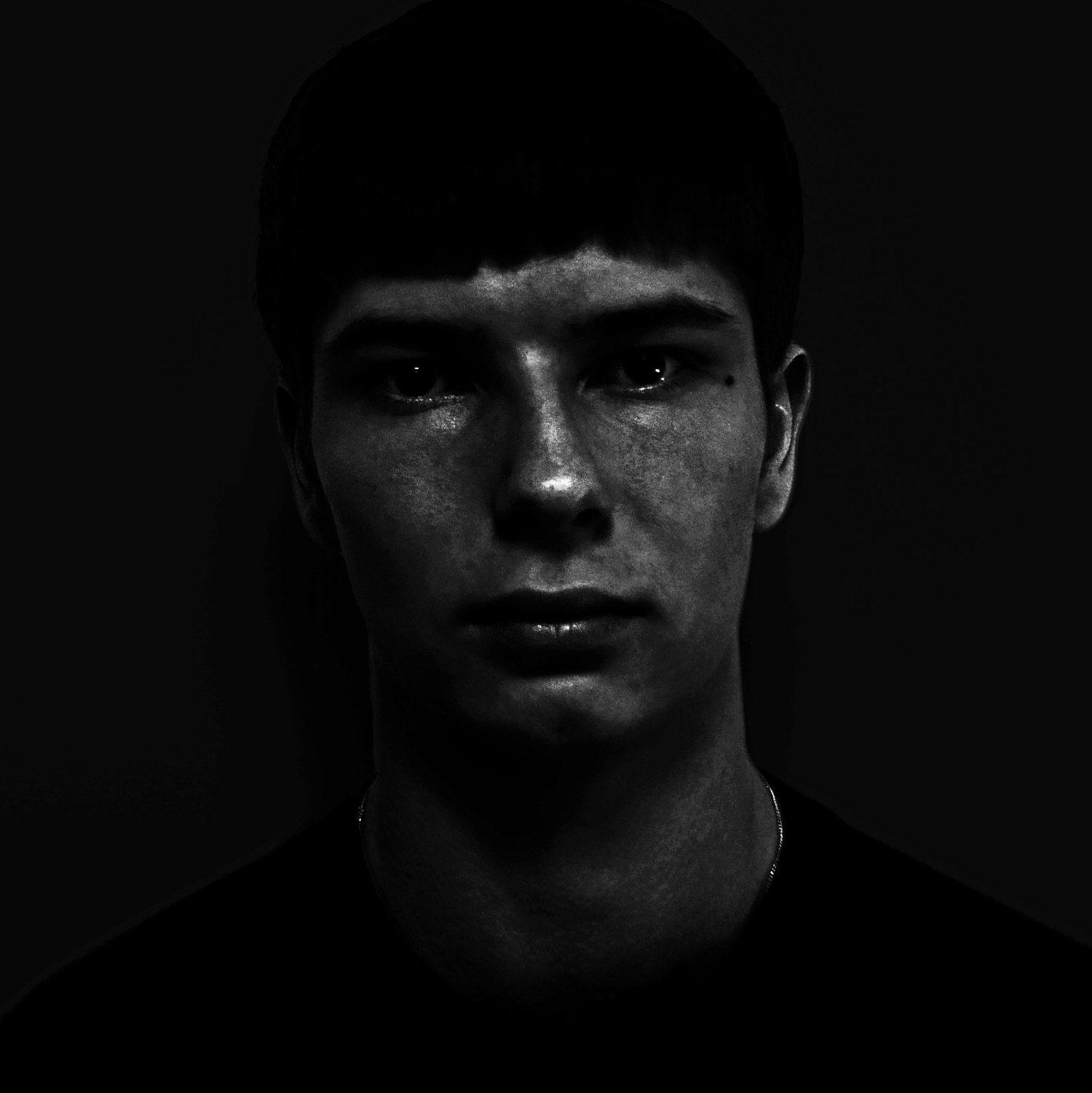 A black and white low-key portrait, one side of the face lit and the rest falling into black