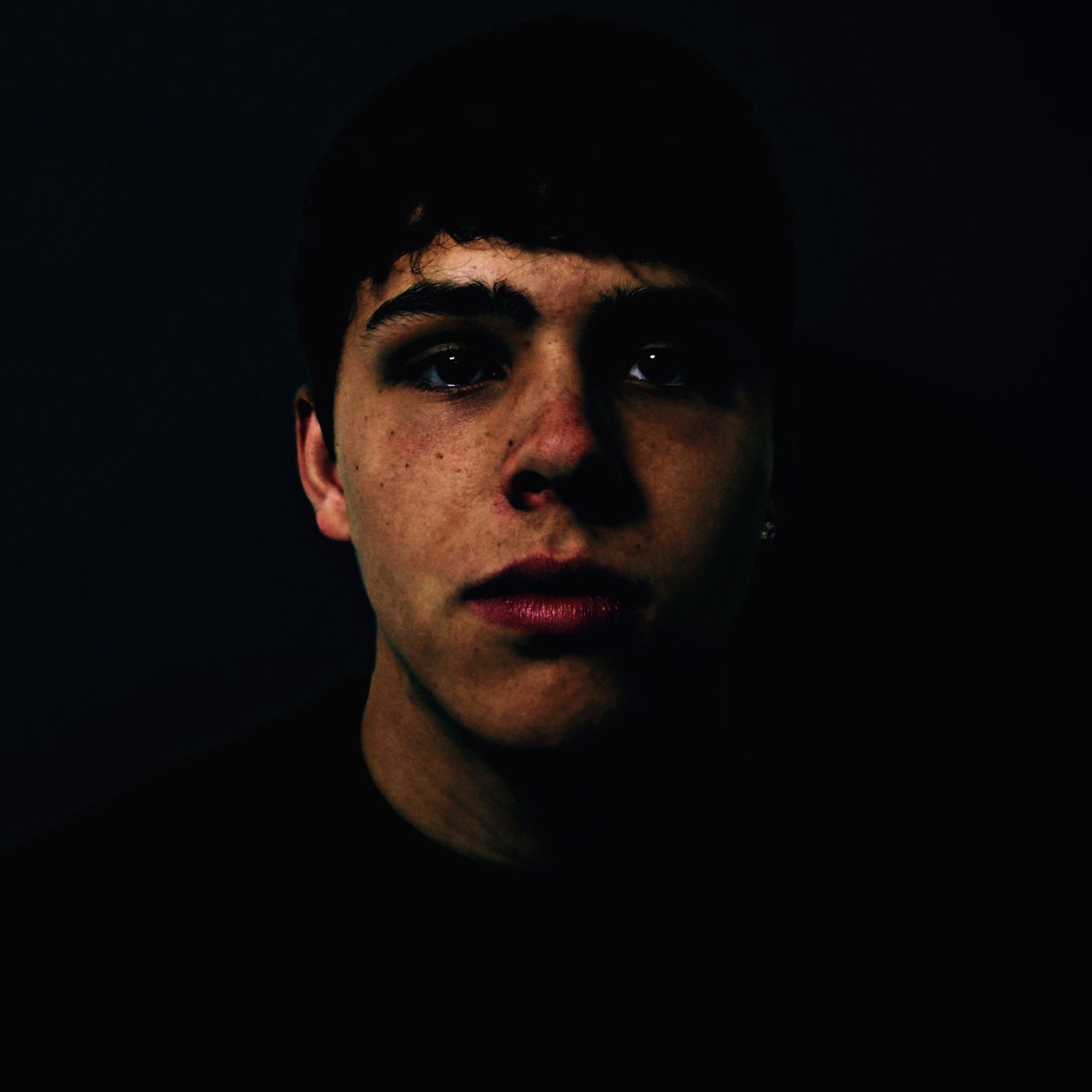 A colour low-key portrait, the face emerging from complete darkness with the eyes catching the light