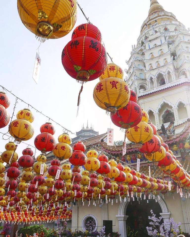 Rows of red and yellow paper lanterns strung above a temple roof against a pale sky