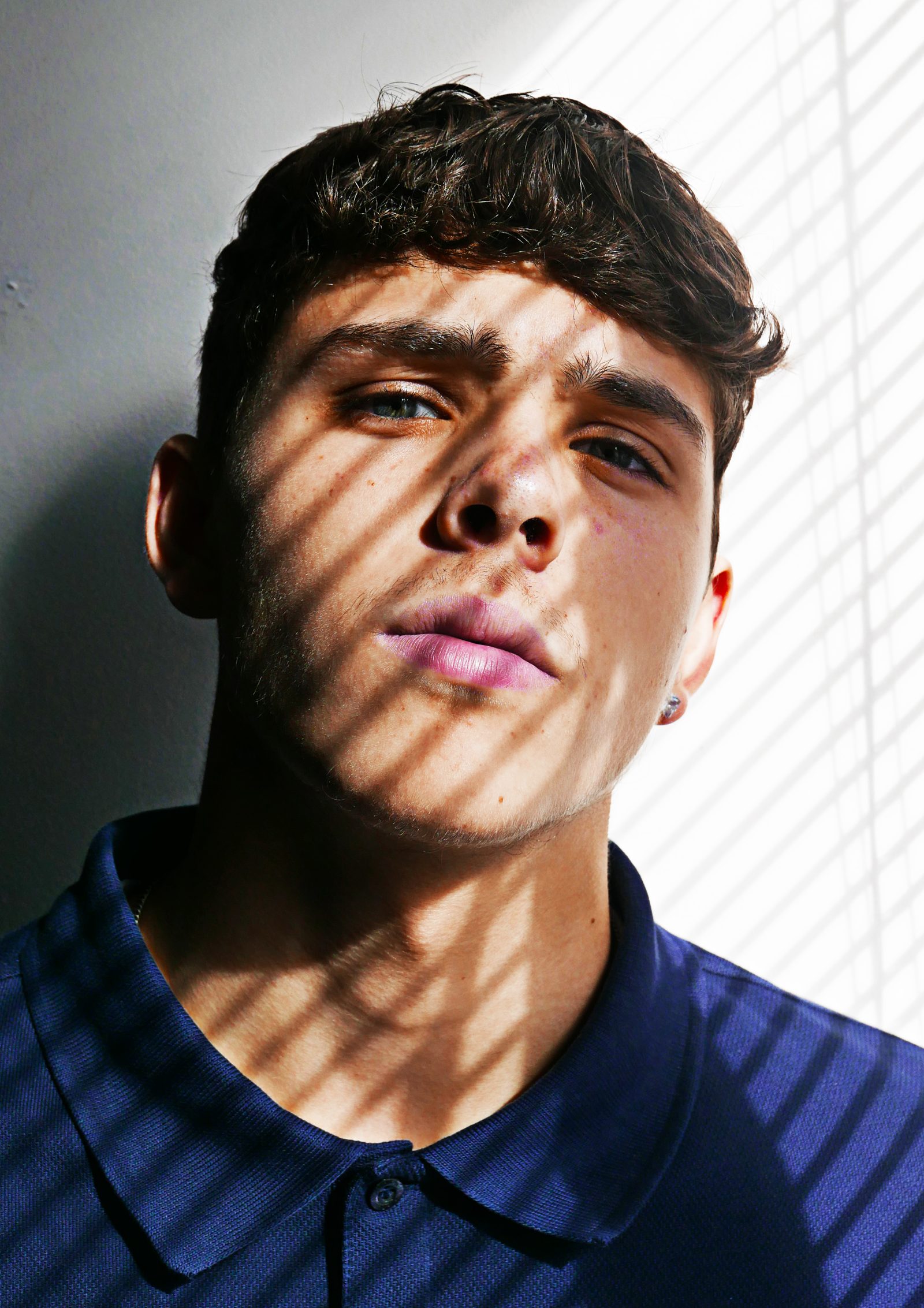 A colour portrait of the same subject in a blue polo shirt, striped shadow across the face, eyes to camera
