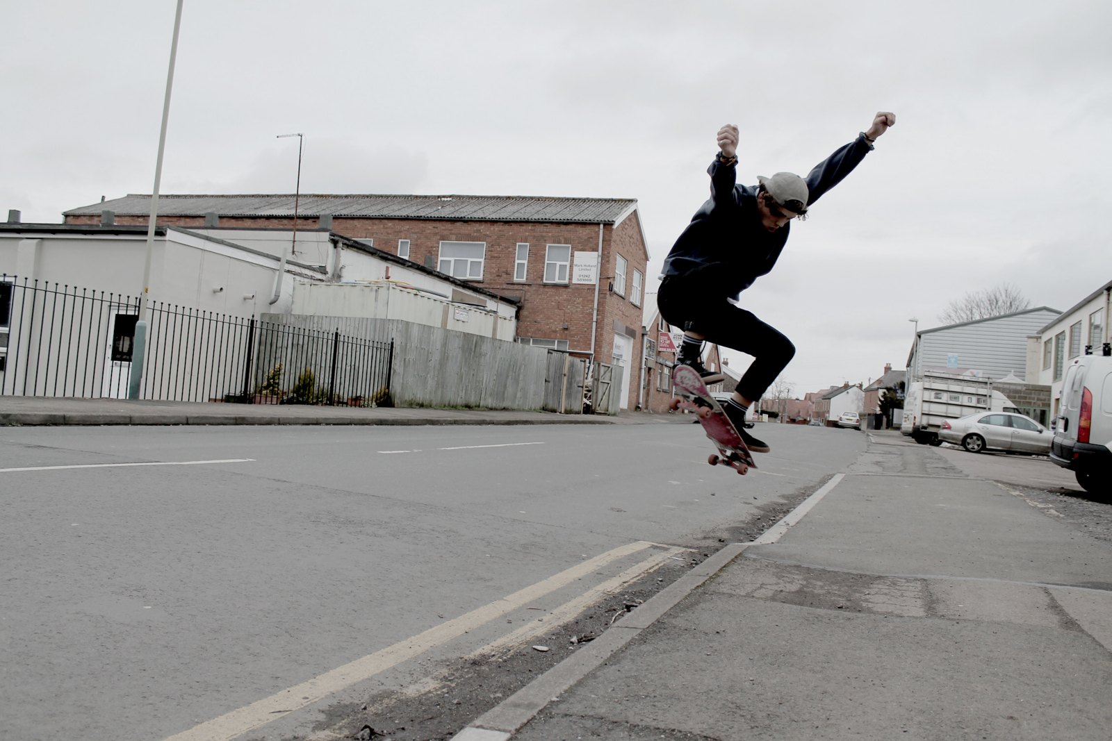 A skater caught mid-kickflip in the middle of an empty industrial street, board turning under him, shot from ground level