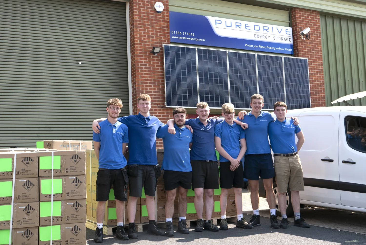 The Puredrive team outside their warehouse with solar panels and stacked product boxes