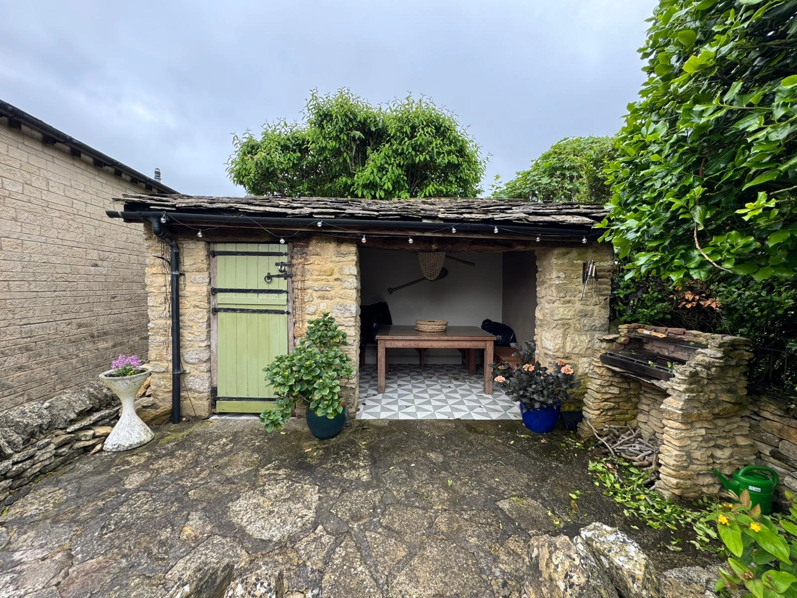 The yard today: an open-fronted stone outbuilding with a green door, a table inside and plants on the flagstones.